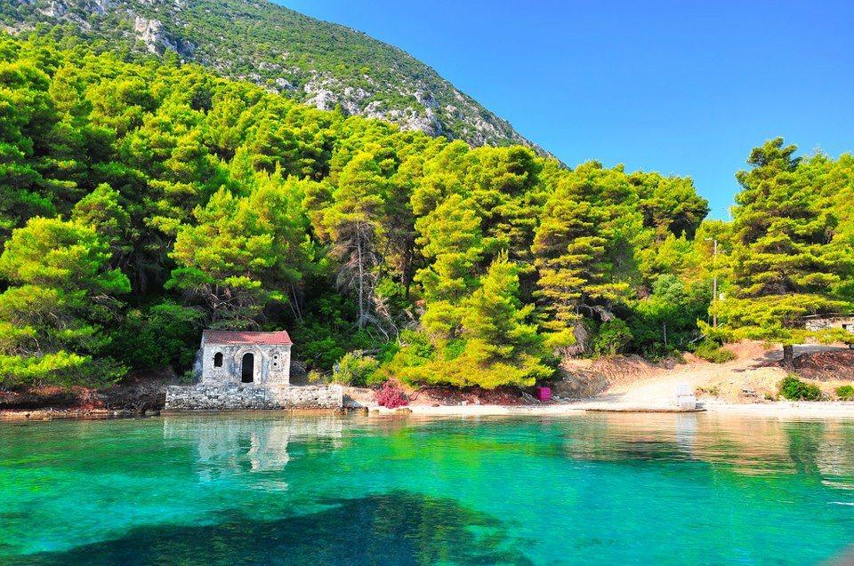Kastos, a stone chapel below pine covered hillside by the water